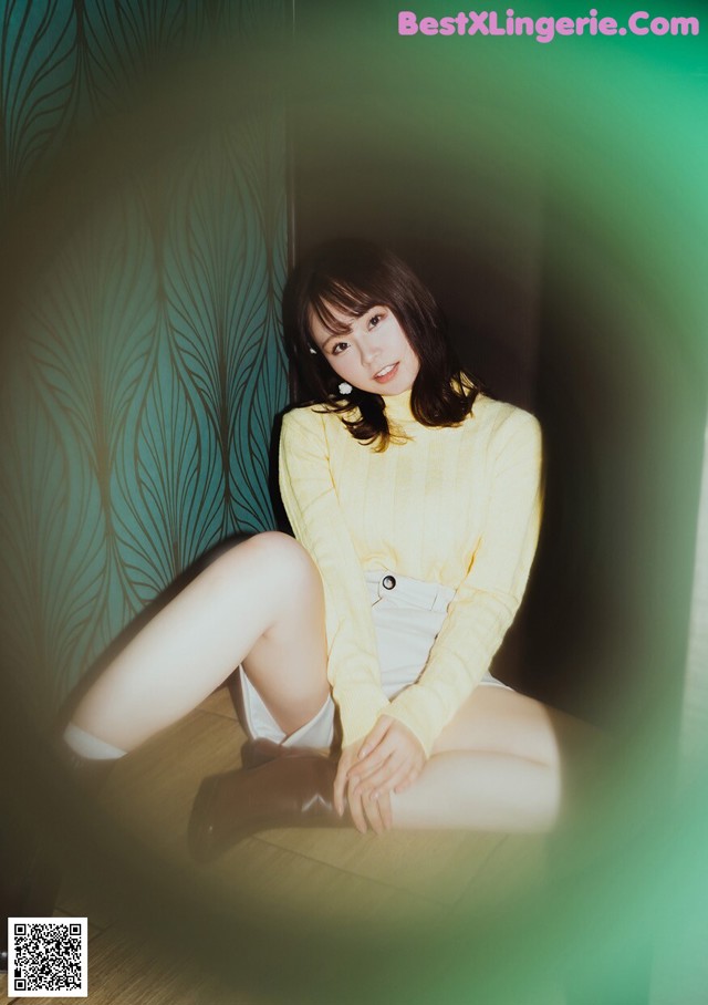 A woman sitting on the floor in a yellow sweater.