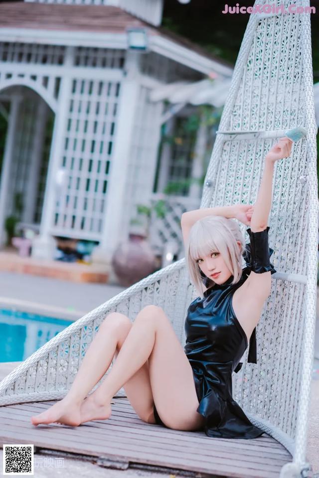 A woman in a black dress sitting on a swing by a pool.