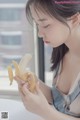 A woman holding a banana in front of a window.