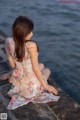 A woman sitting on a rock by the water.