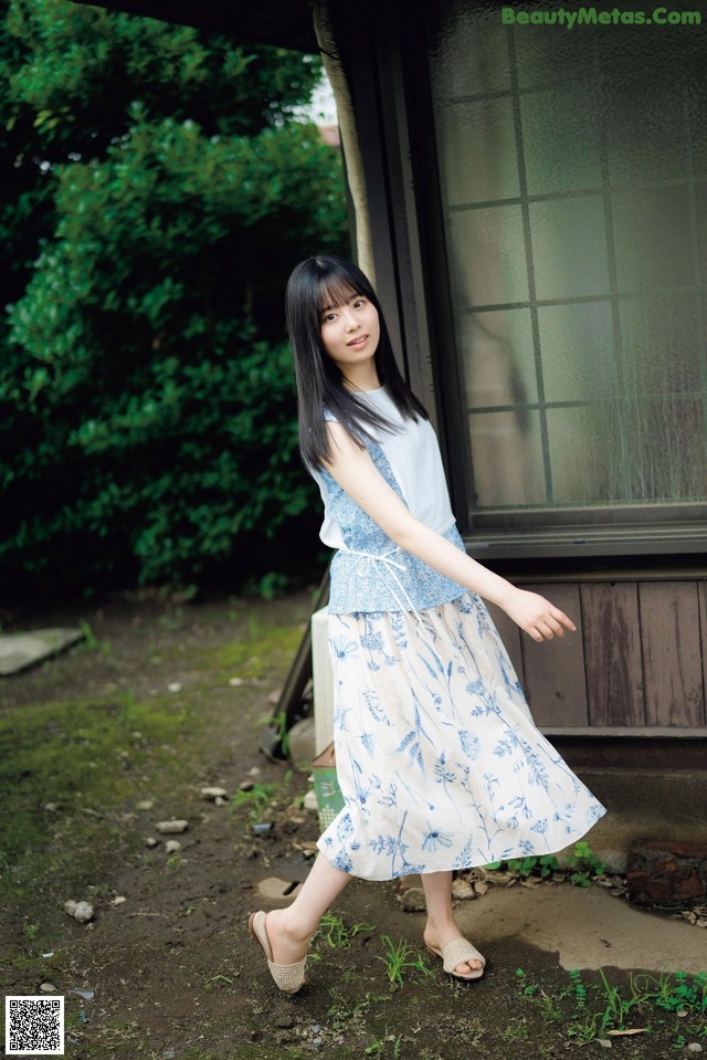A woman standing in front of a house wearing a blue and white dress.