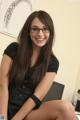 A young woman wearing glasses sitting on a desk.