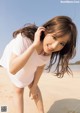 A woman in a white shirt is posing on the beach.