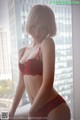 A woman in a red lingerie posing by a window.