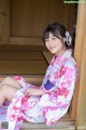 A woman in a pink and white kimono sitting on a wooden bench.