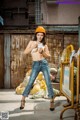 A woman wearing a hard hat and jeans posing for a picture.