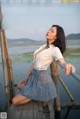 A woman in a white shirt and plaid skirt sitting on a wooden dock.